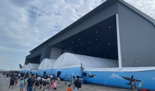Airshow crowd outside hangar and white tents with airplane-themed decorations.